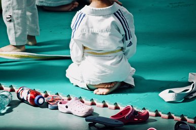 Eine junge Judoka sitzt mit dem Rücken zur Kamera. Hinter ihr liegen Schuhe und Trinkflaschen.