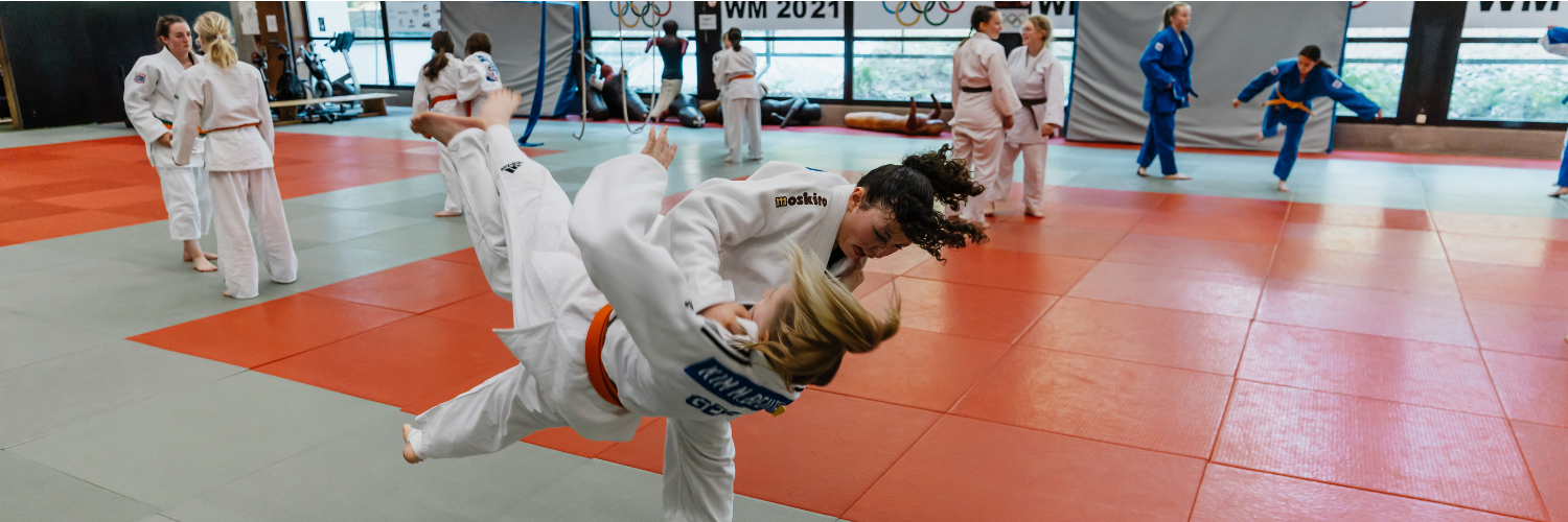 Zwei Judoka im Trainingswettkampf. Im Hintergrund trainieren weitere Judoka.