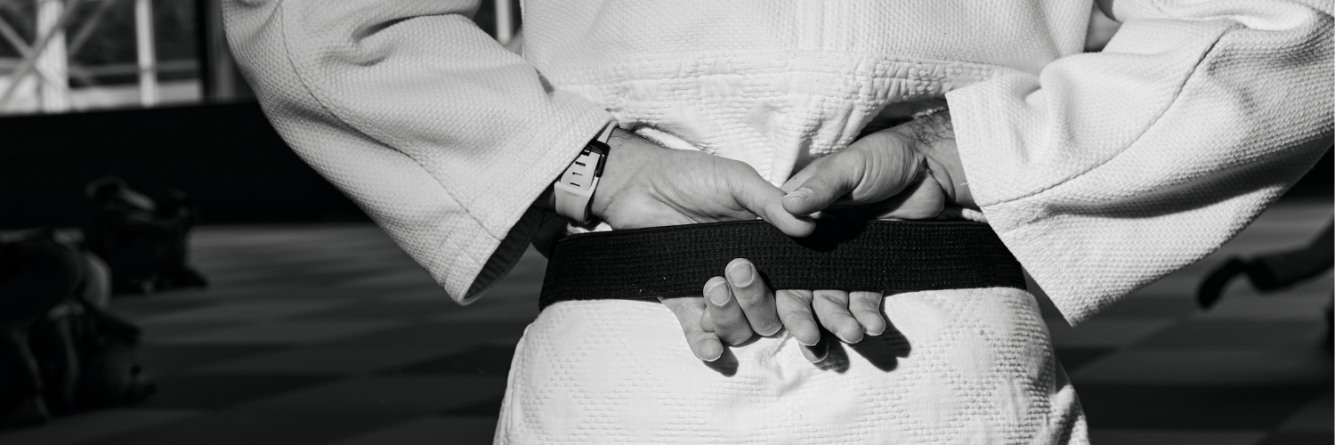 Detailaufnahme der Haende eines Judoka, die seinen schwarzen Guertel umfassen.