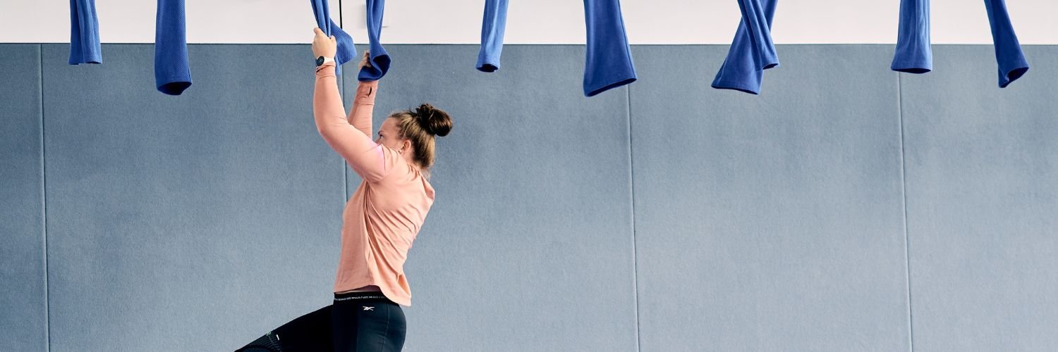 Eine Sportlerin hangelt sich an blauen Seilen durch eine Turnhalle.
