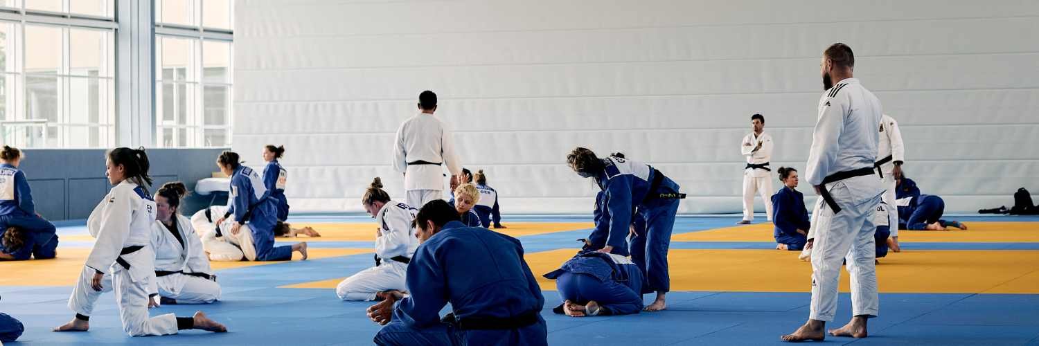 Judoka beim Training in einer großen Sporthalle.