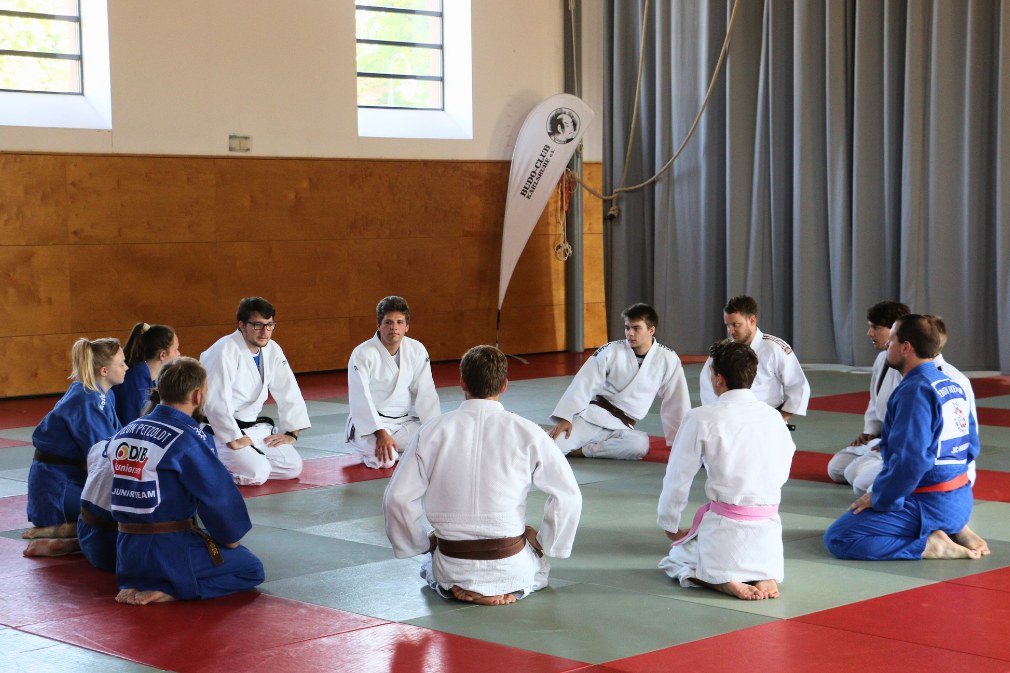 Judoka sitzen kniend im Kreis auf dem Boden.