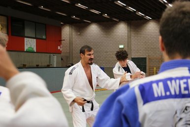Ein Judotrainer erklaert den umstehenden Judokas etwas.