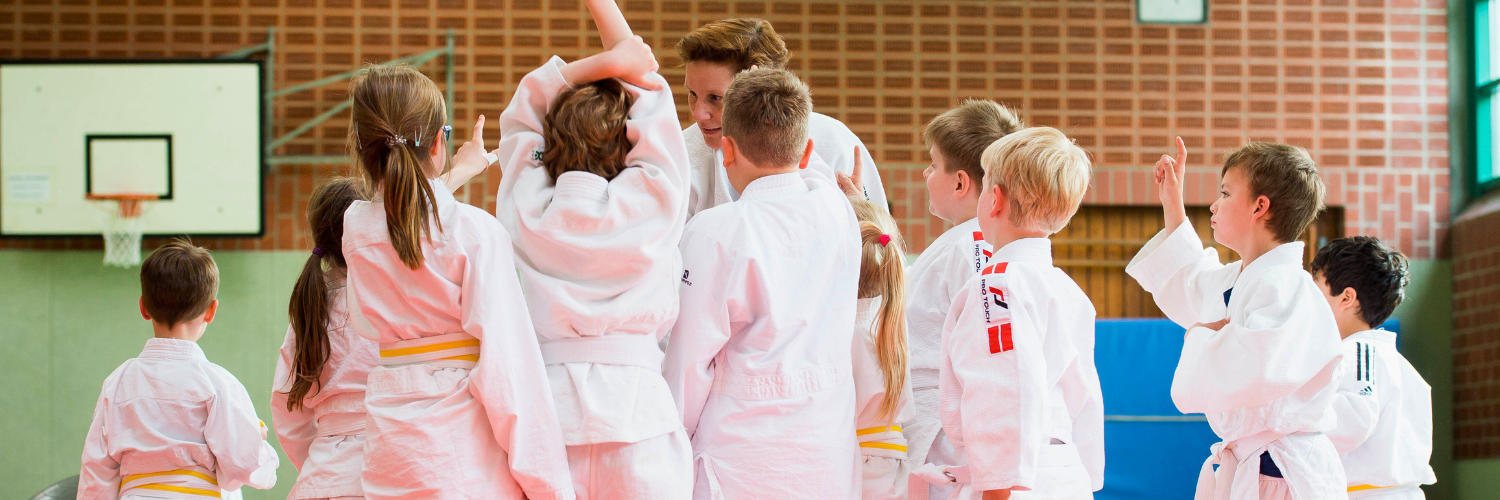 Viele Kinder stehen um einen Judotrainer herum und reden mit ihm.